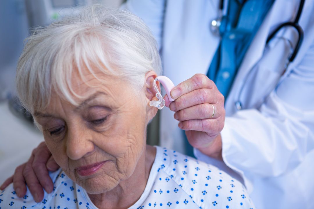 Doctor inserting hearing aid in senior patient ear Photo from Pikwizard